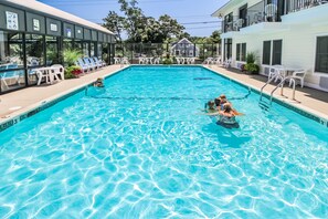 A swimming pool with clear blue water, surrounded by lounge chairs and a building with large windows.