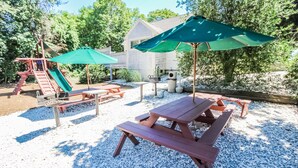 Un patio trasero con mesas de picnic, un tobogán y una casa al fondo.