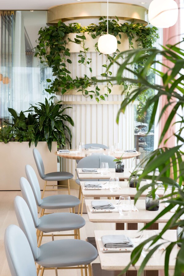 A modern restaurant with a long dining table, several chairs, and a variety of plants. - Fairmont Pacific Rim (Vancouver)