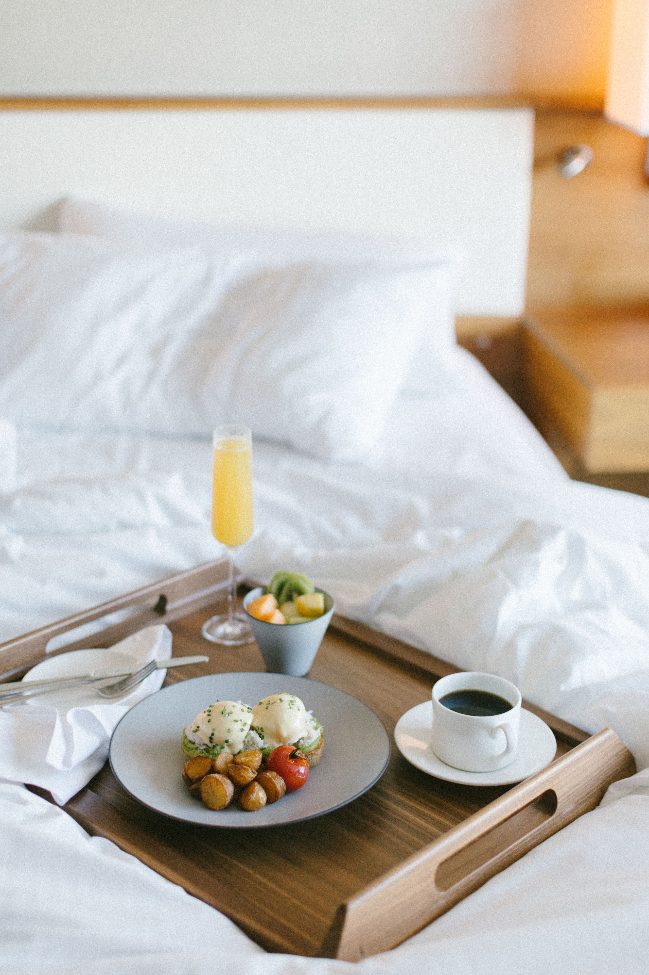 A breakfast tray with eggs benedict, fruit, and coffee on a bed.