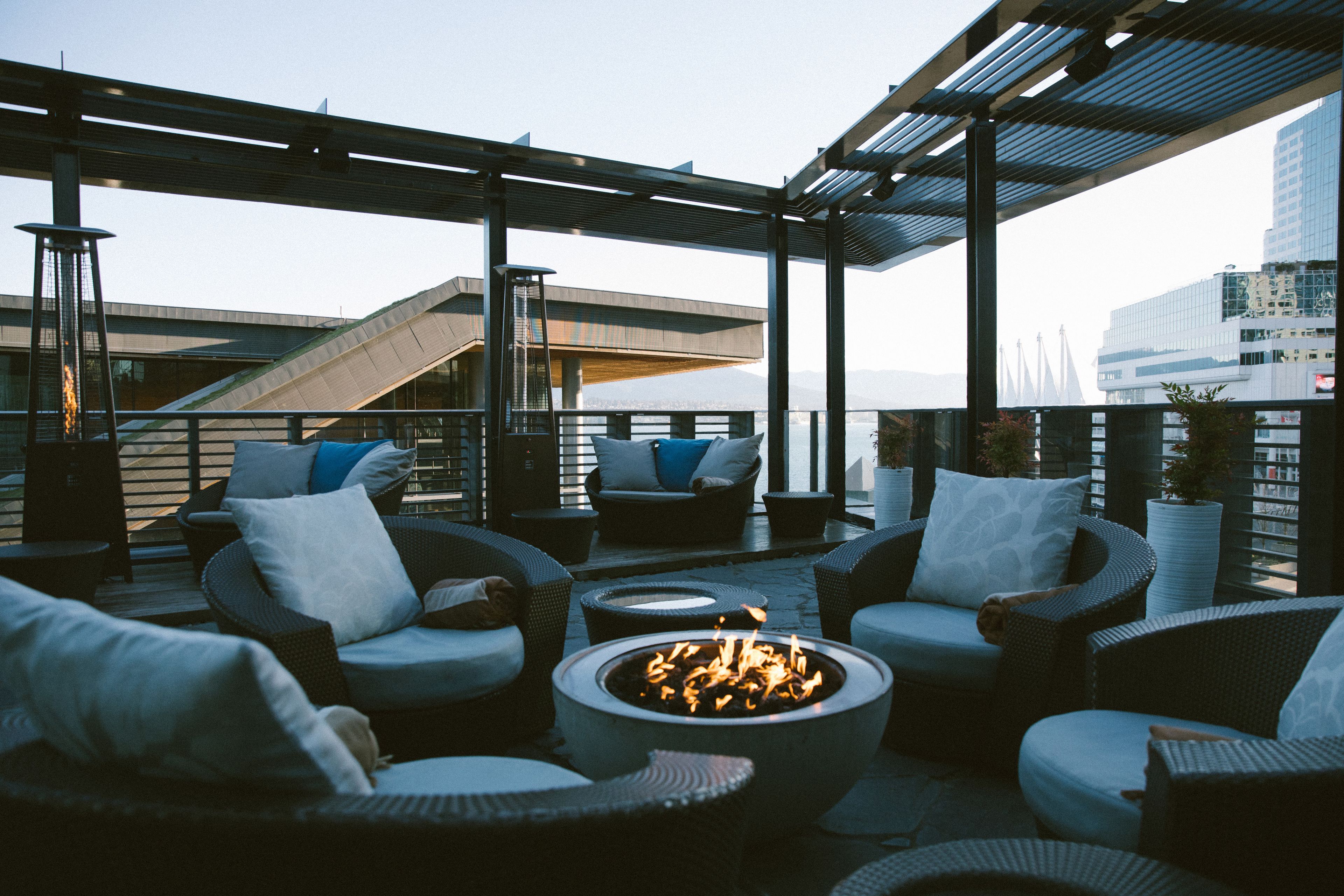 Un salón en la azotea con mobiliario de mimbre, una chimenea central y vistas a un puente y al paisaje urbano.