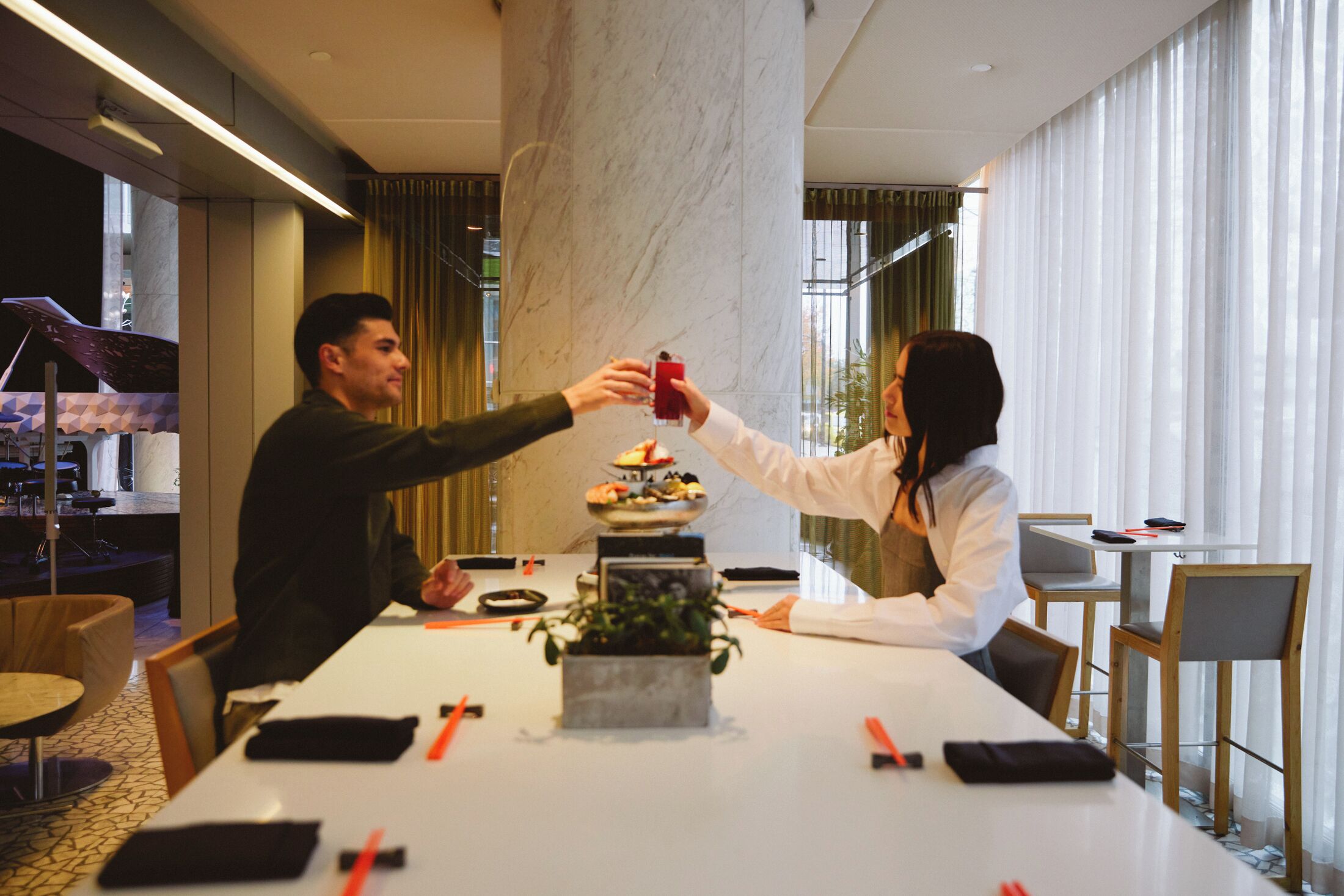 Habitación de hotel moderna con un pilar de mármol, una mesa de comedor con un centro de mesa y vistas de la ciudad a través de amplios ventanales.