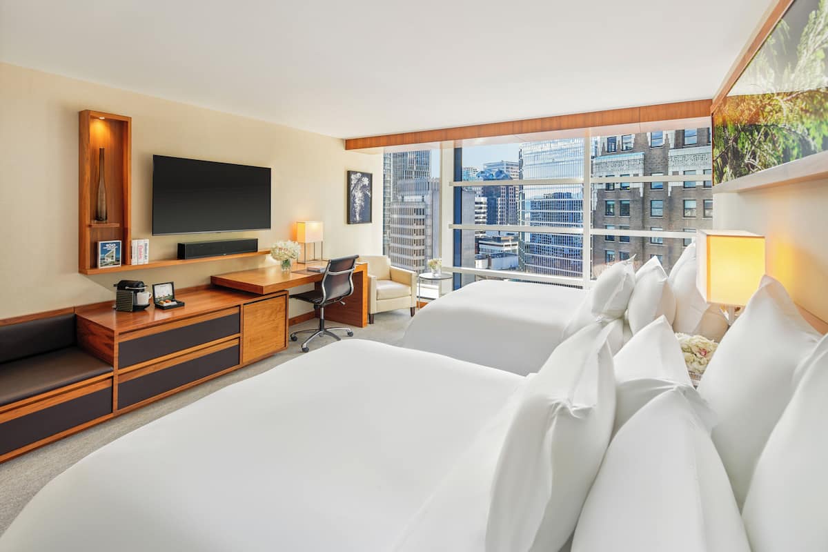 A hotel room with a large bed, a desk with a chair, a television, and a window with a city view.