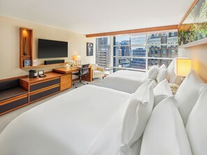Quarto de hotel com uma cama grande, uma escrivaninha com cadeira, uma televisão e uma janela com vista para a cidade.