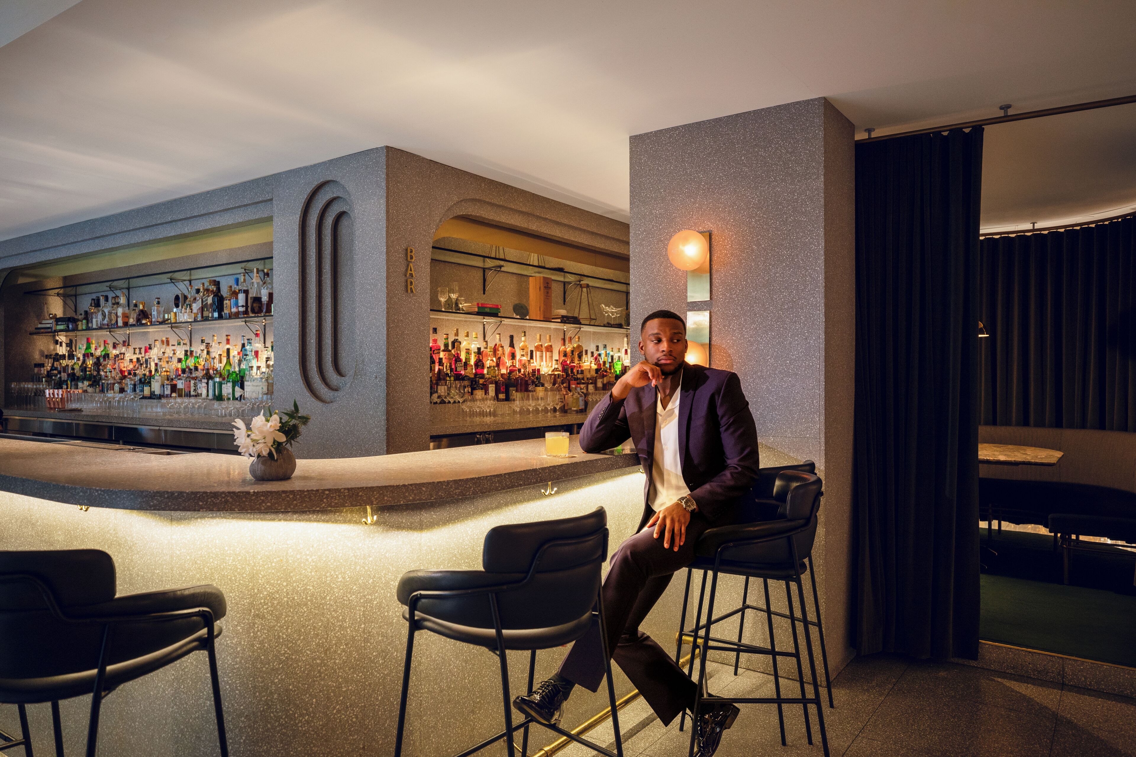 A bar area with a counter and stools, a bar stocked with bottles, and a decorative wall.