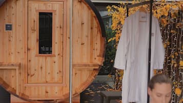 A wooden sauna with a red umbrella, a white robe hanging, and a person in a bathtub.
