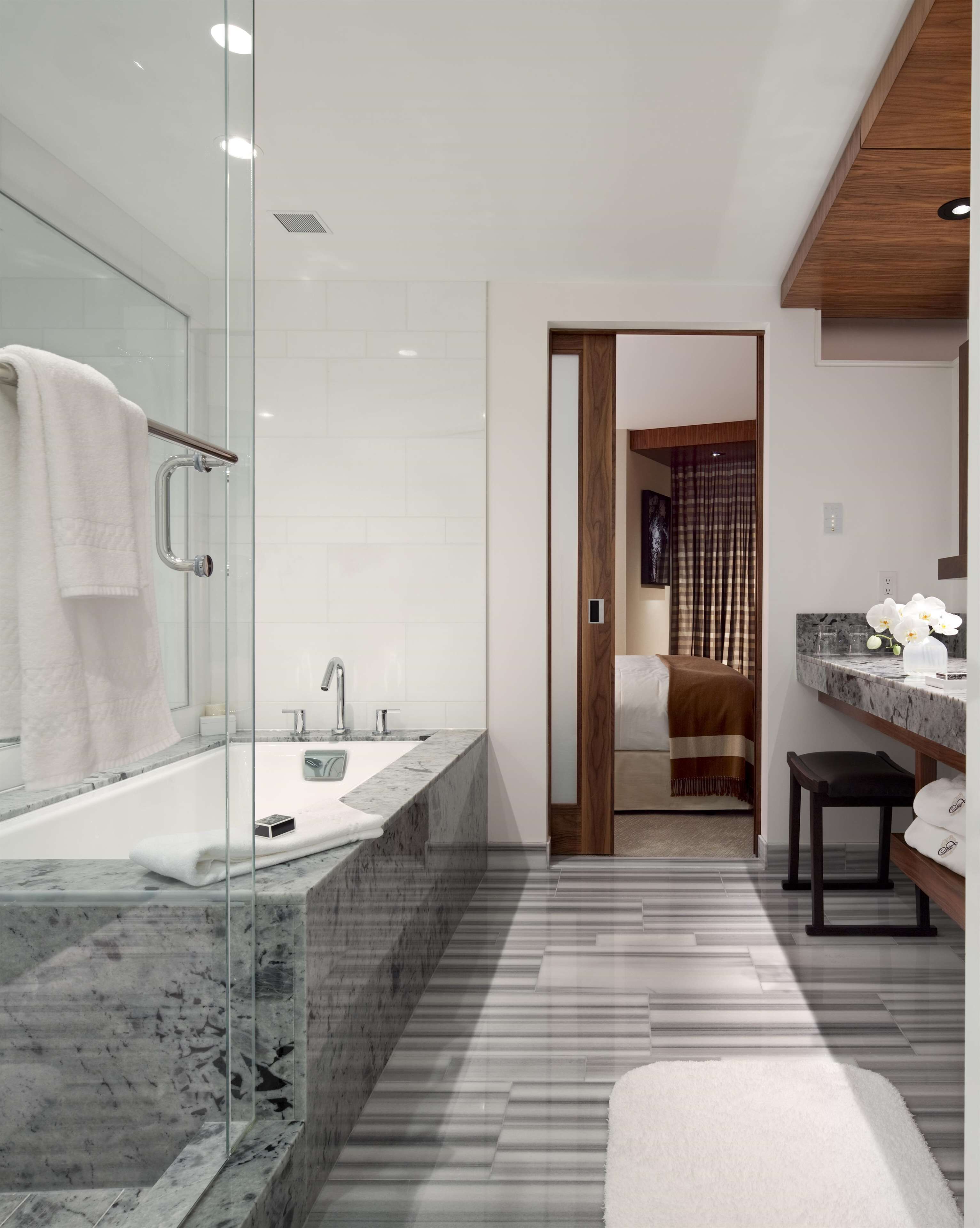 Un baño moderno con cabina de ducha de vidrio, lavamanos de mármol y tocador de madera.