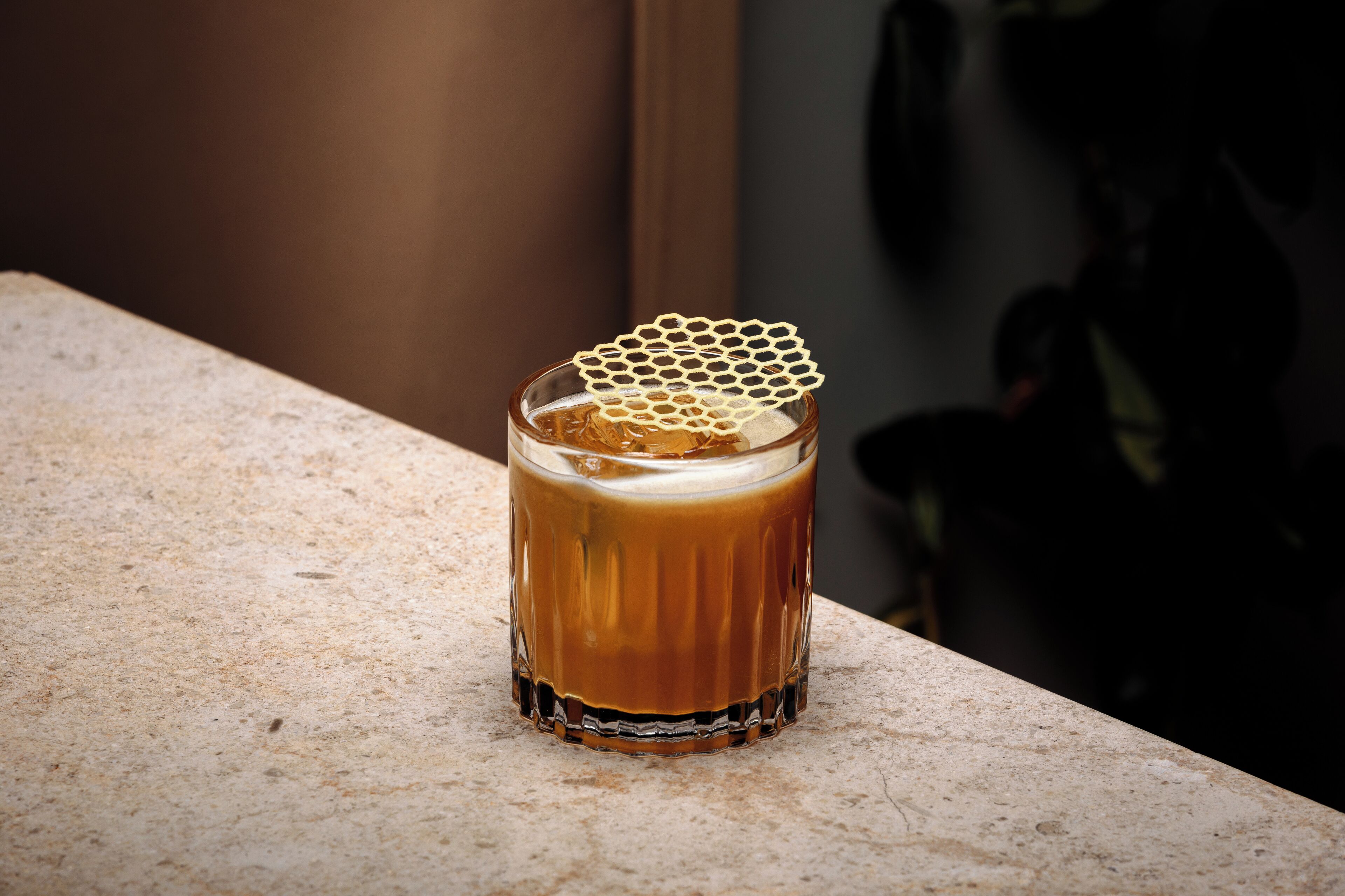Un vaso de bebida color ámbar con una decoración de panal sobre una encimera texturizada.