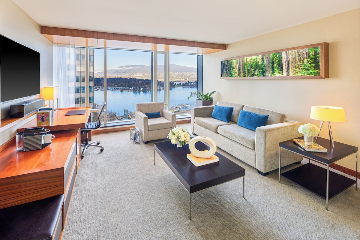 A modern hotel room with a large window offering a scenic view of a lake and mountains.