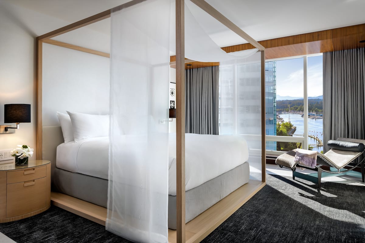A modern hotel room with a large bed, a sitting area with a view, and a wooden floor.