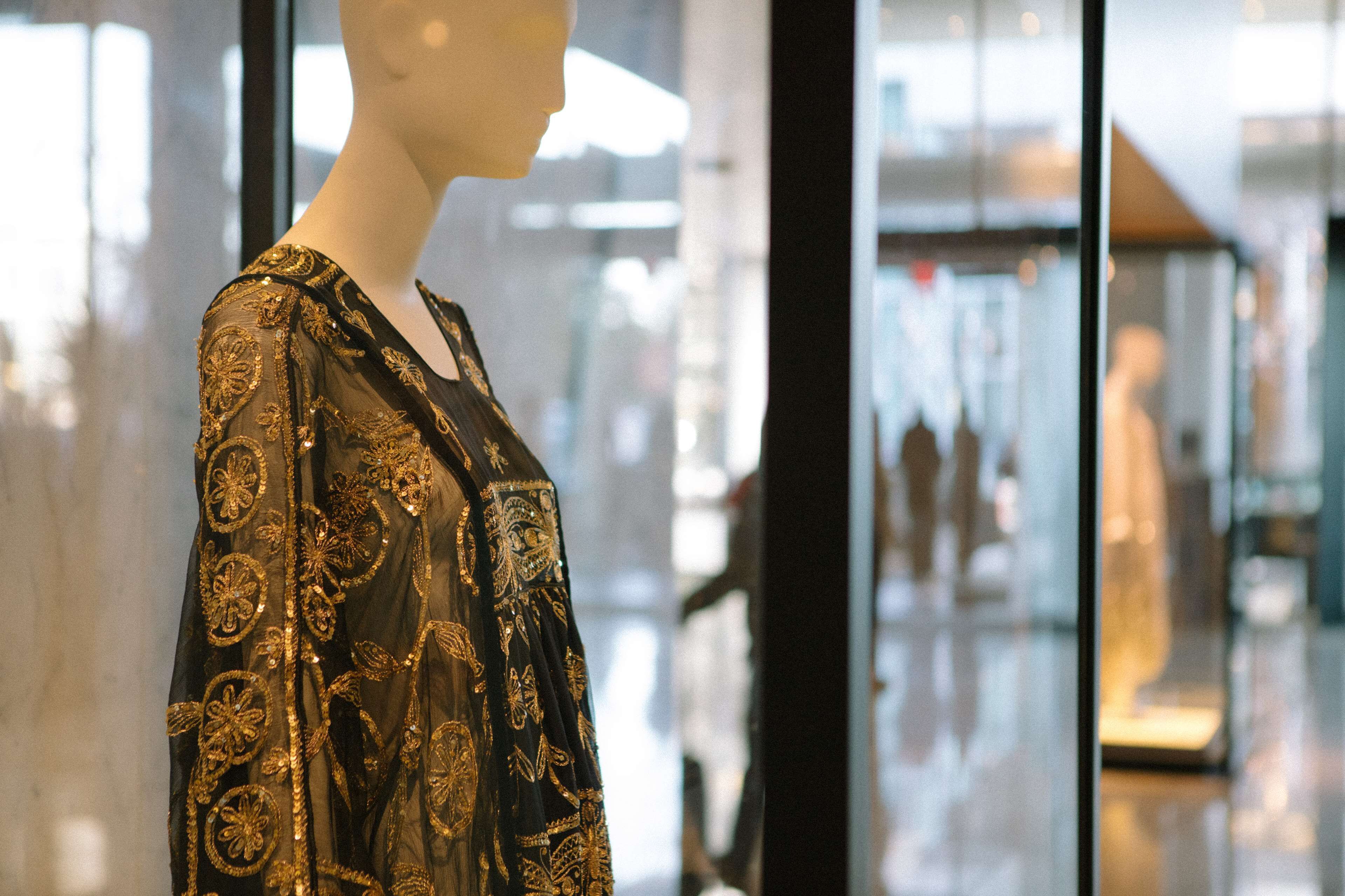 Un maniquí en una finestra d'una botiga mostra un vestit negre amb brodat daurat.
