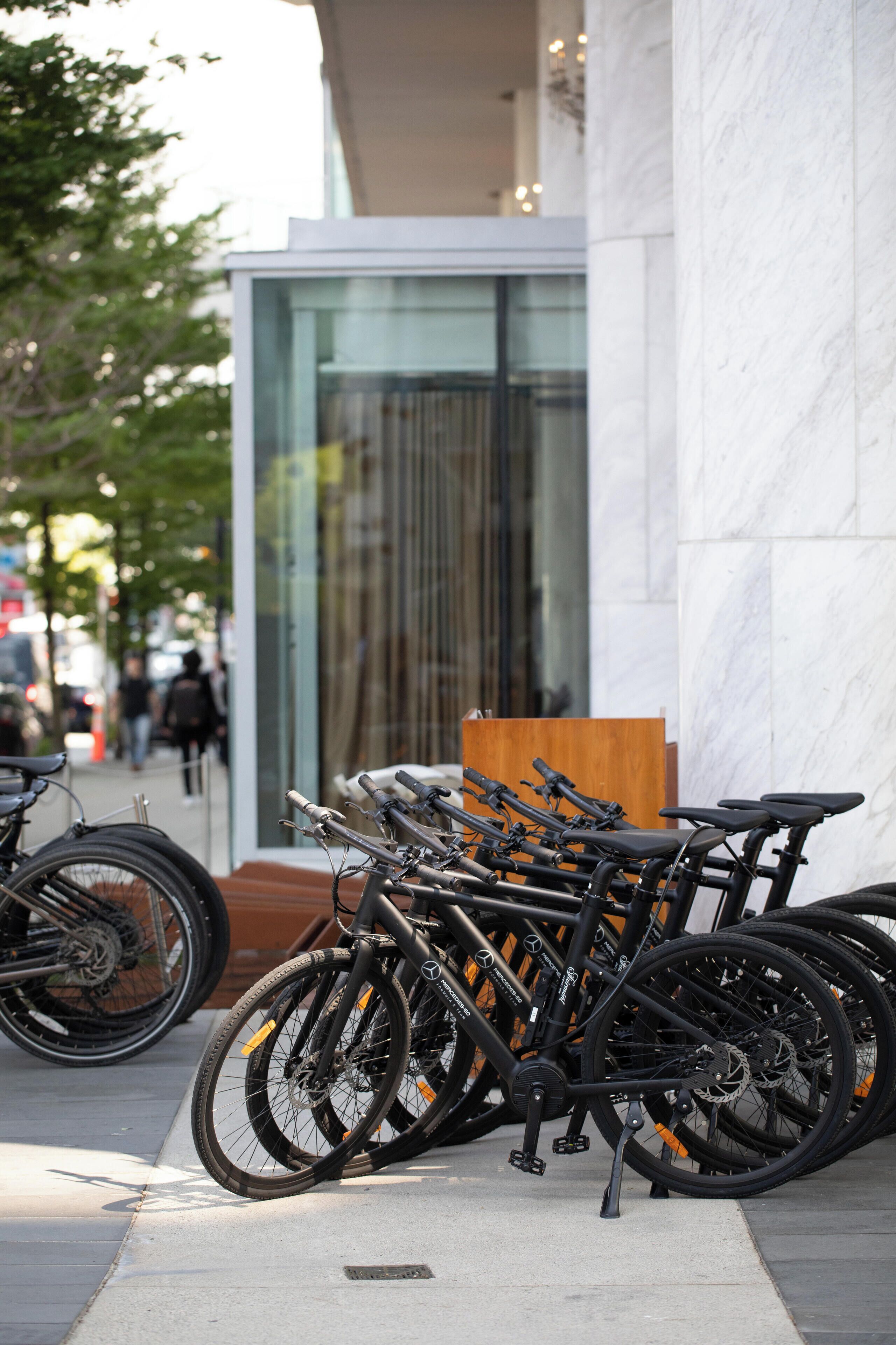A row of bicycles parked against a building with a glass facade.