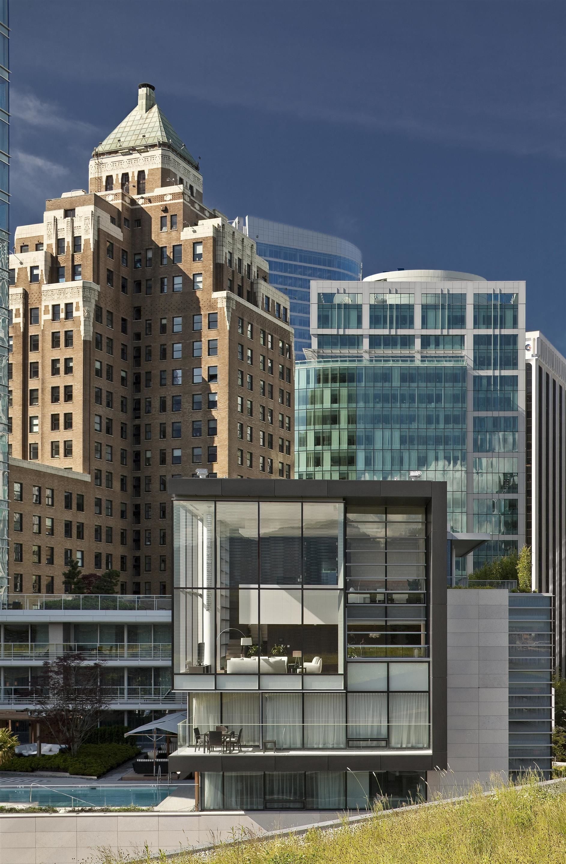 A modern building with a glass facade, a pool area, and a view of a historic building with a dome.