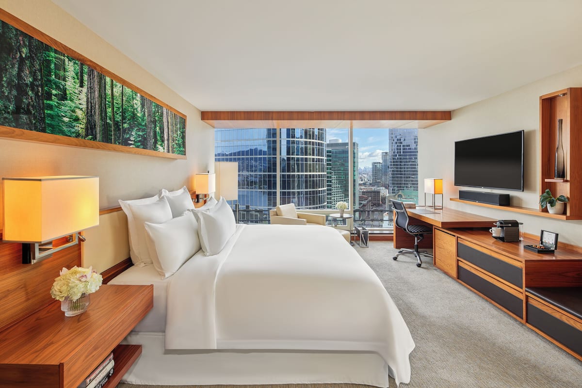 A modern hotel room with a large bed, a desk, a television, and a city view.