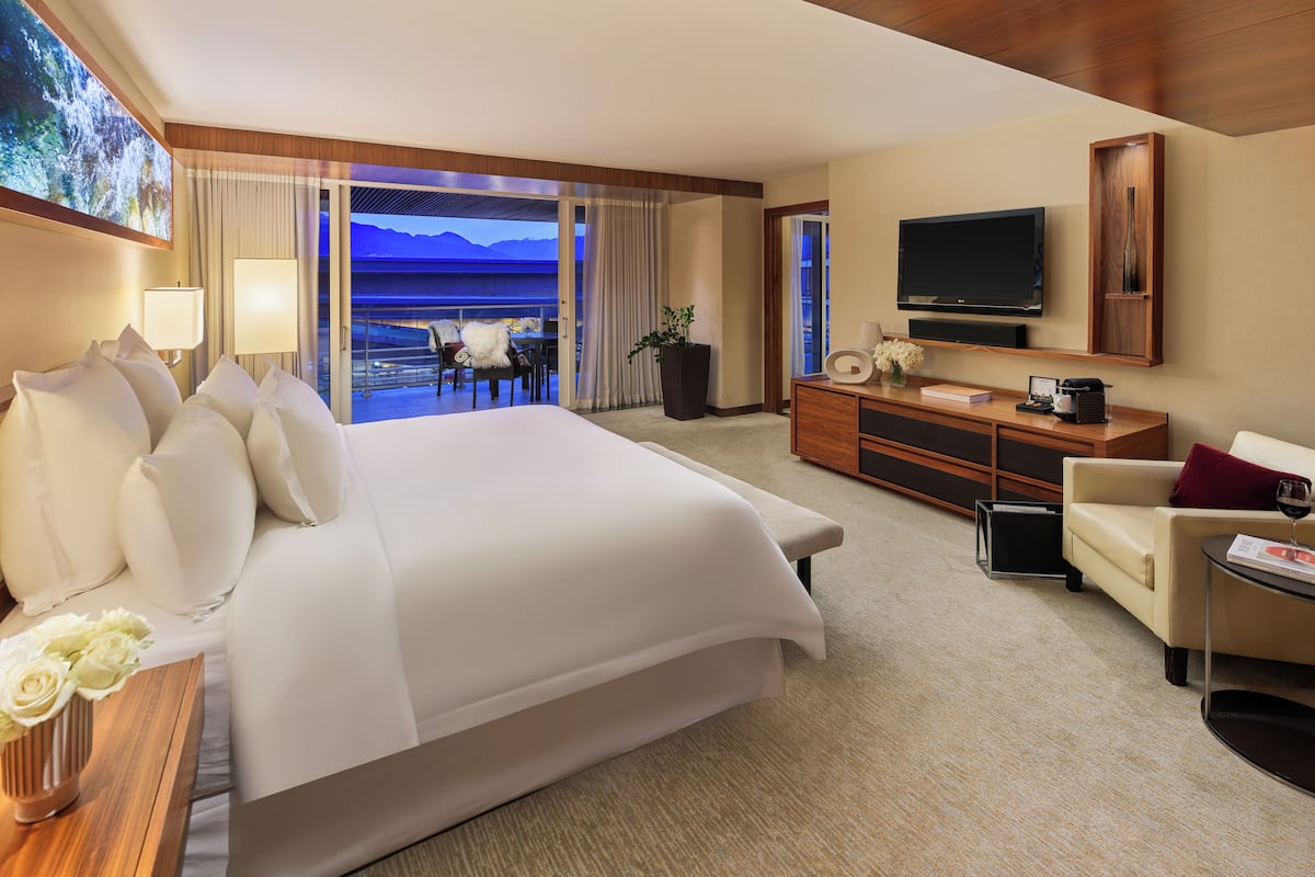 A hotel room with a large bed, a TV, a seating area, and a view of the mountains.