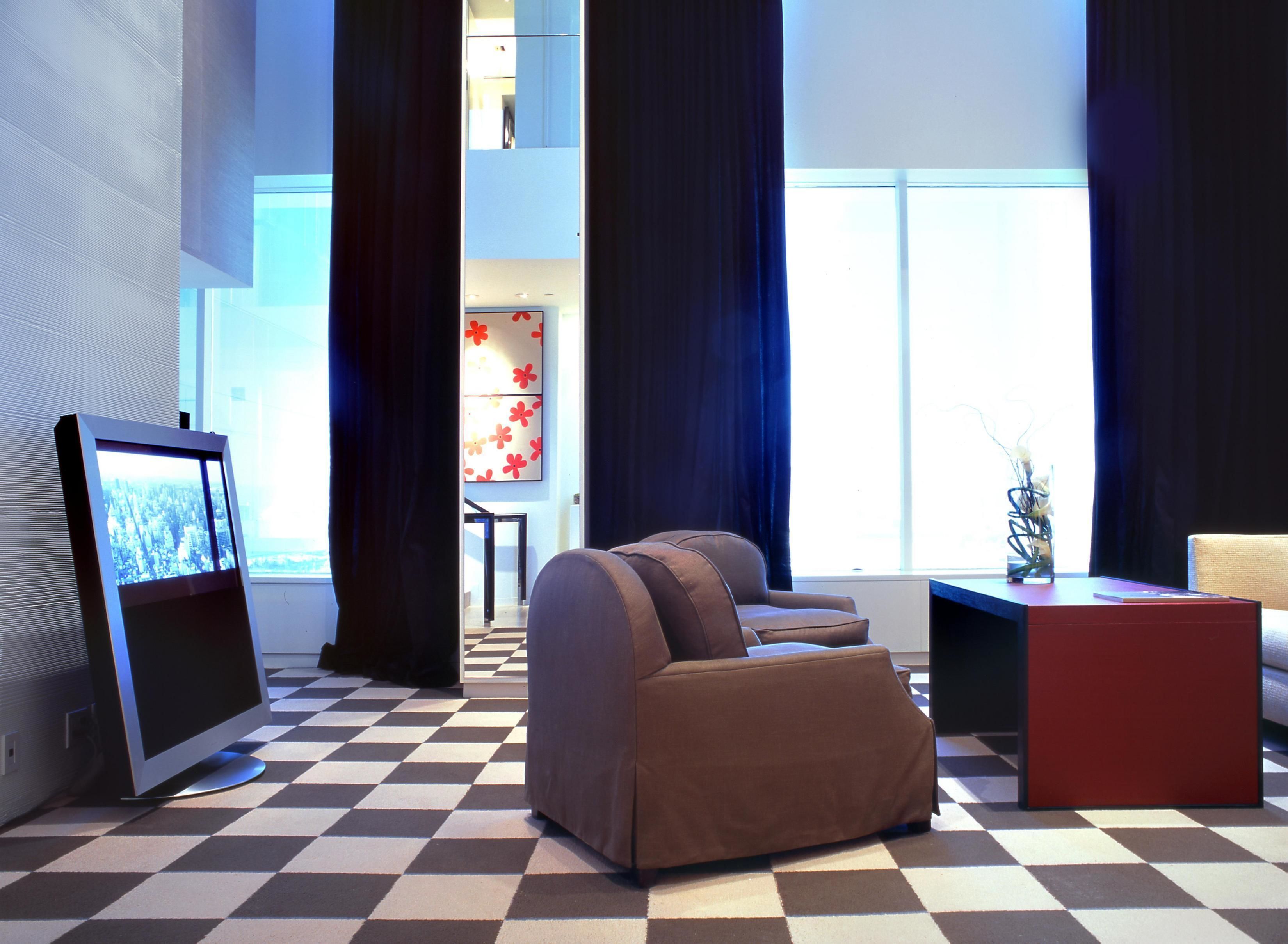 A modern living room with a checkered floor, a brown sofa, a red side table, and a television on a stand.