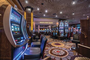 A hotel room with a television displaying a cityscape, a bed, a bedside table with a vase of flowers, and a mirror on the wall. at The SKYLOFTS at MGM Grand