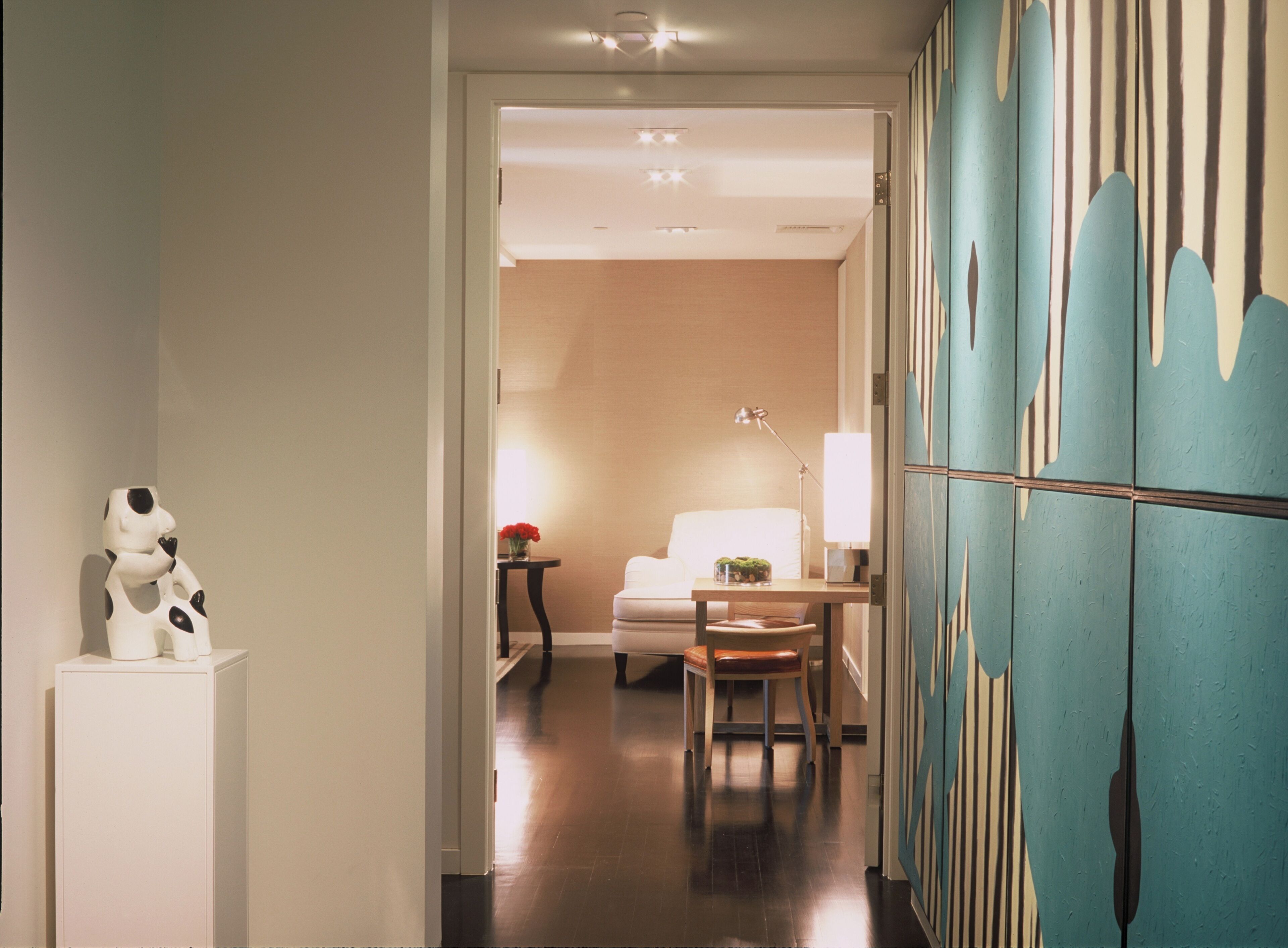 A hotel room with a bed, a desk with a lamp, a chair, and a decorative cow sculpture.