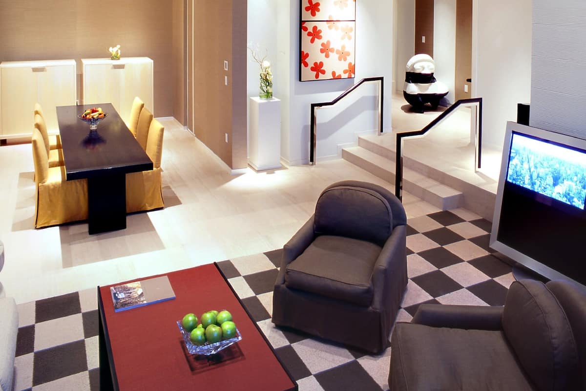 Un moderno vestíbulo de hotel con zona de comedor, asientos, una escalera y una pantalla de televisión.