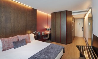 A modern hotel room with a large bed, a desk, and a wardrobe.