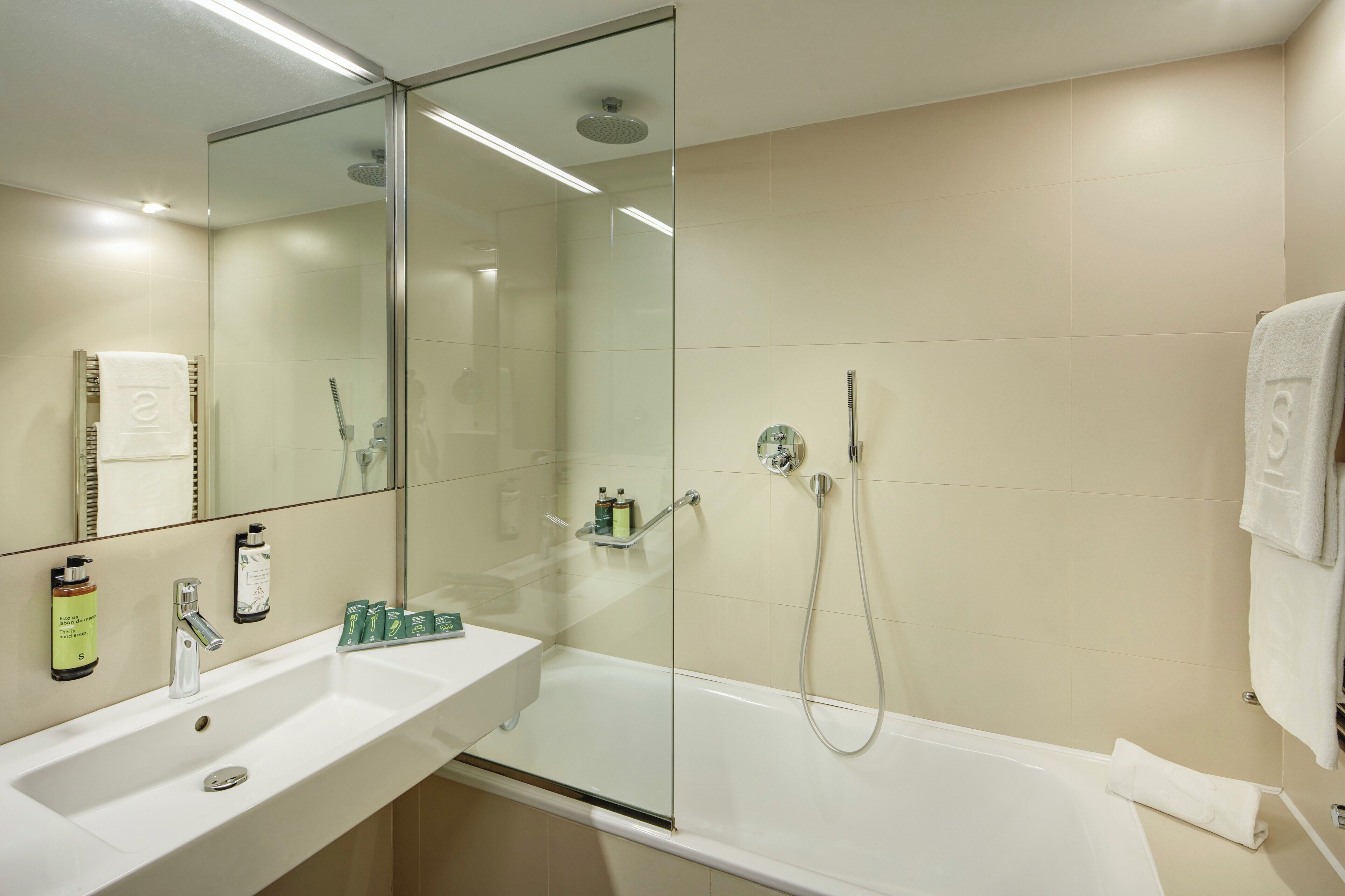 Un baño moderno con ducha envuelta en vidrio, un lavabo blanco y un espejo grande.