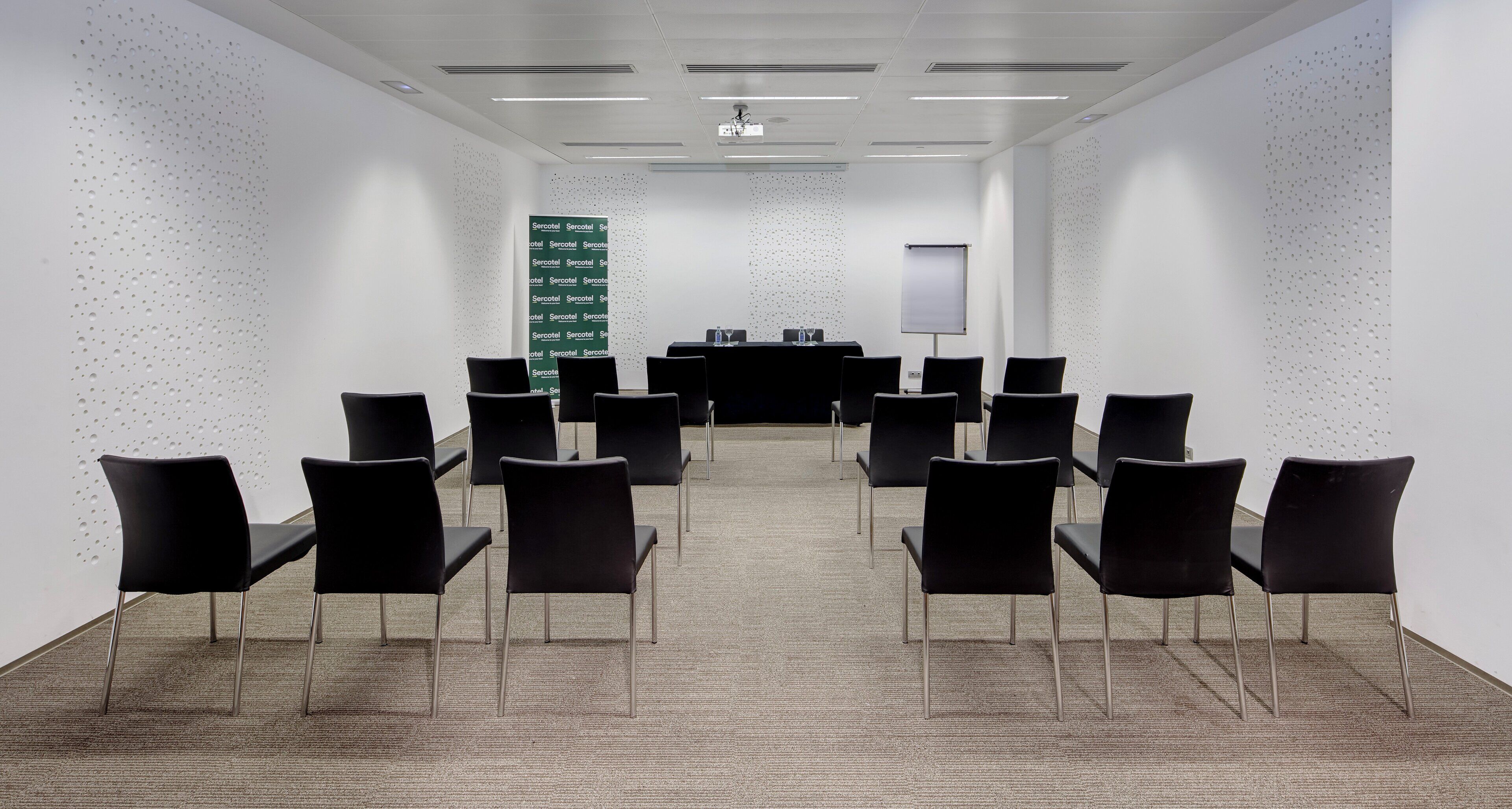 A conference room with a long table, black chairs, a projector screen, and a whiteboard.