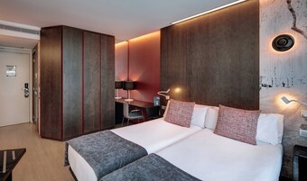 Una habitación de hotel moderna con una cama grande, un escritorio, un armario y una lámpara fijada a la pared.