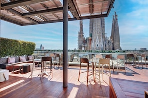 A rooftop terrace with wooden flooring, seating arrangements, and a view of the Sagrada Familia. - Sercotel Rosellon (Barcelona)