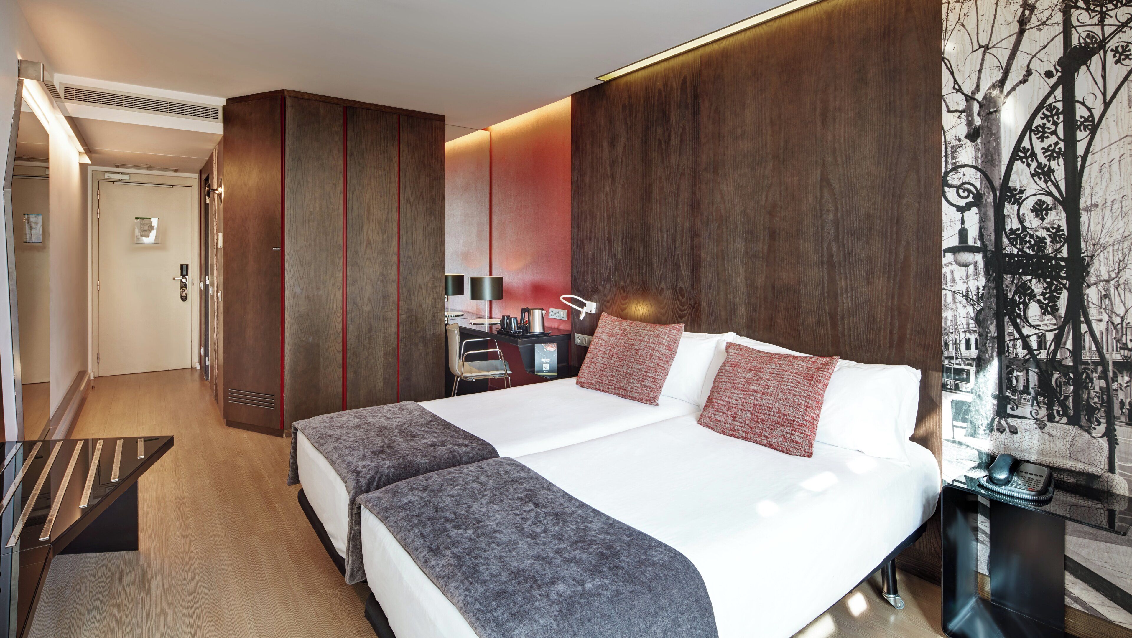 Una habitación de hotel con una cama grande, un escritorio con una lámpara y vistas de la ciudad a través de una ventana.