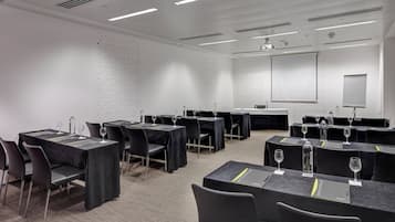 Un salón de conferencias con mesas y sillas, una pantalla de proyector y una pizarra.