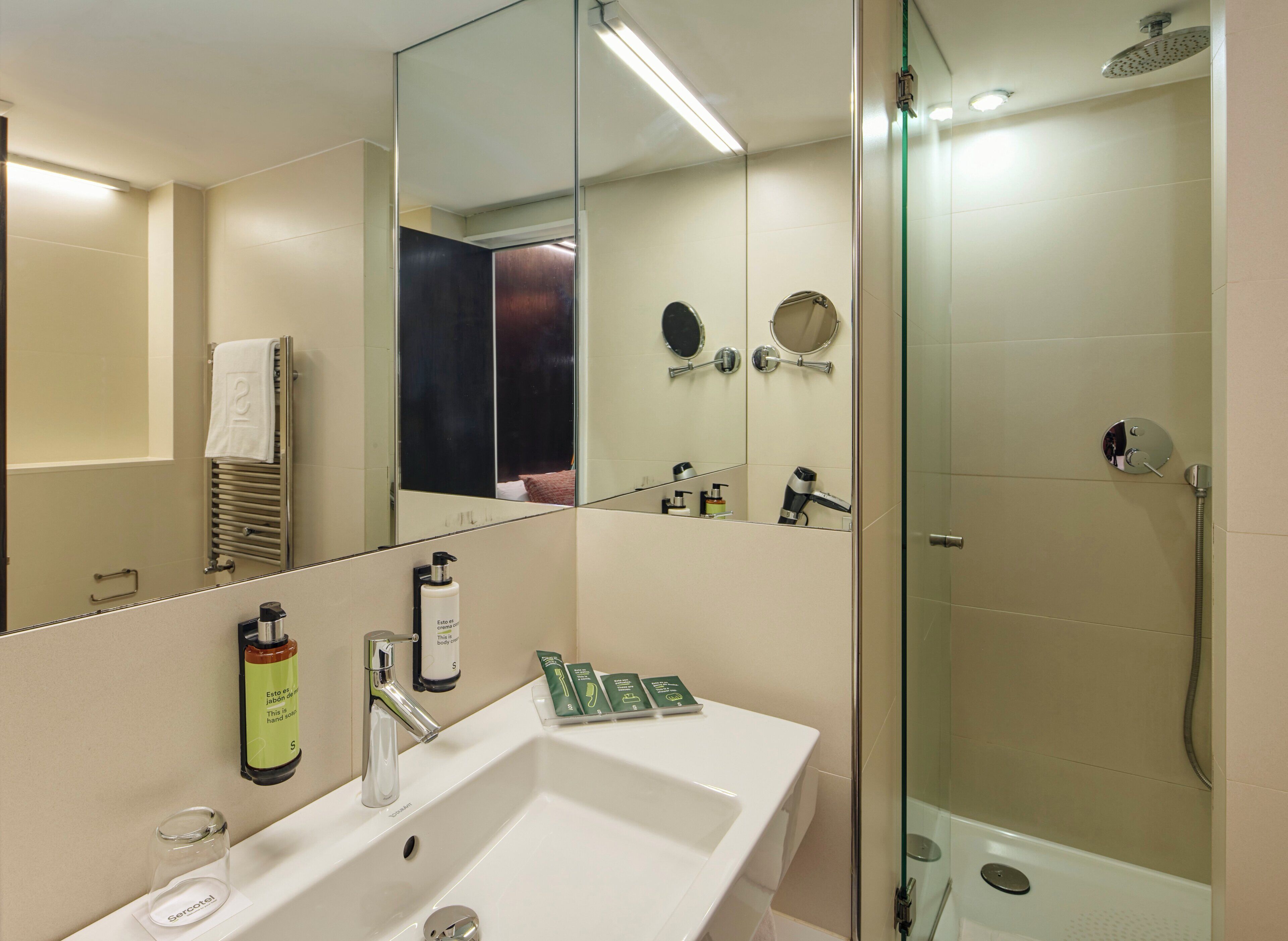 Un baño moderno con un espejo grande, un lavamanos, una ducha y un perchero para toallas.
