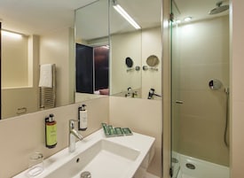 A modern bathroom with a large mirror, a sink, a shower, and a towel rack.