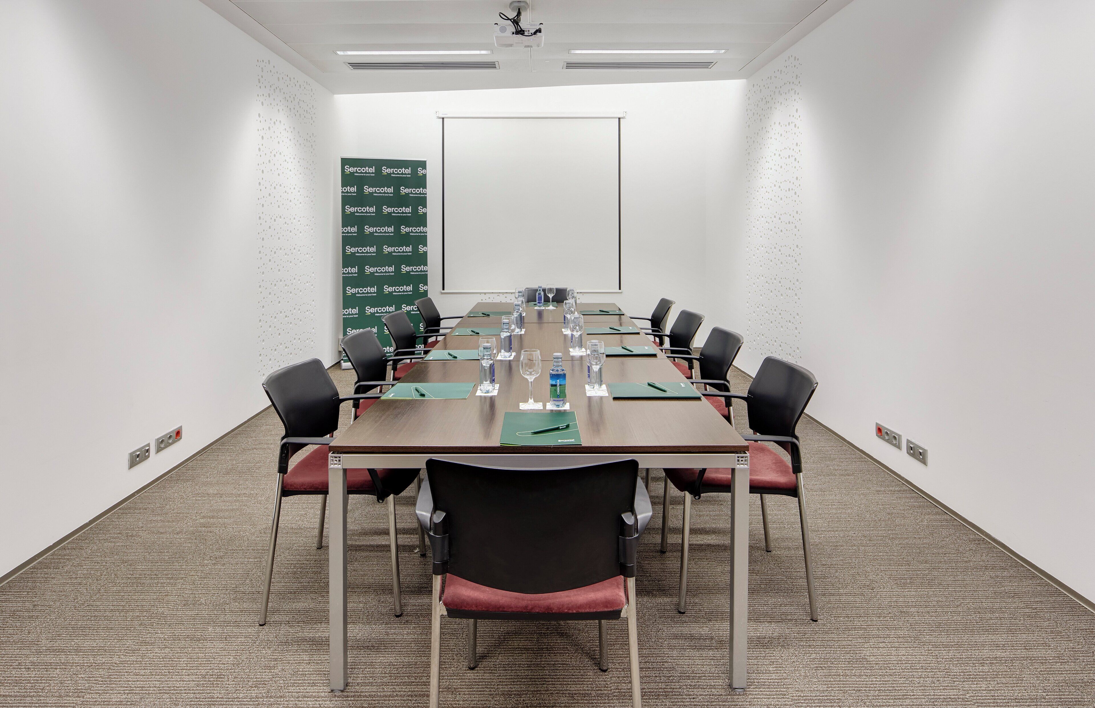 A conference room with a long table, chairs, water bottles, and a projector screen.