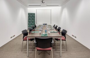A conference room with a long table, chairs, water bottles, and a projector screen.