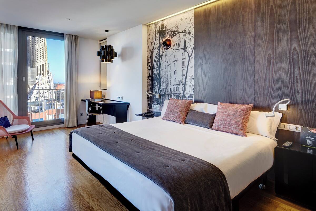 Une chambre d’hôtel moderne, dotée d’un grand lit, d’un bureau, d’une chaise et offrant une vue sur le paysage urbain par la fenêtre.
