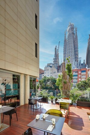 An outdoor seating area with tables and chairs, a view of a tall building with intricate architecture, and a clear blue sky. - Sercotel Rosellon (Barcelona)