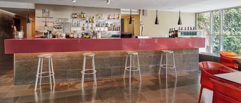 Uma área de bar moderna com balcão vermelho, vários taburetes e uma variedade de garrafas e copos.