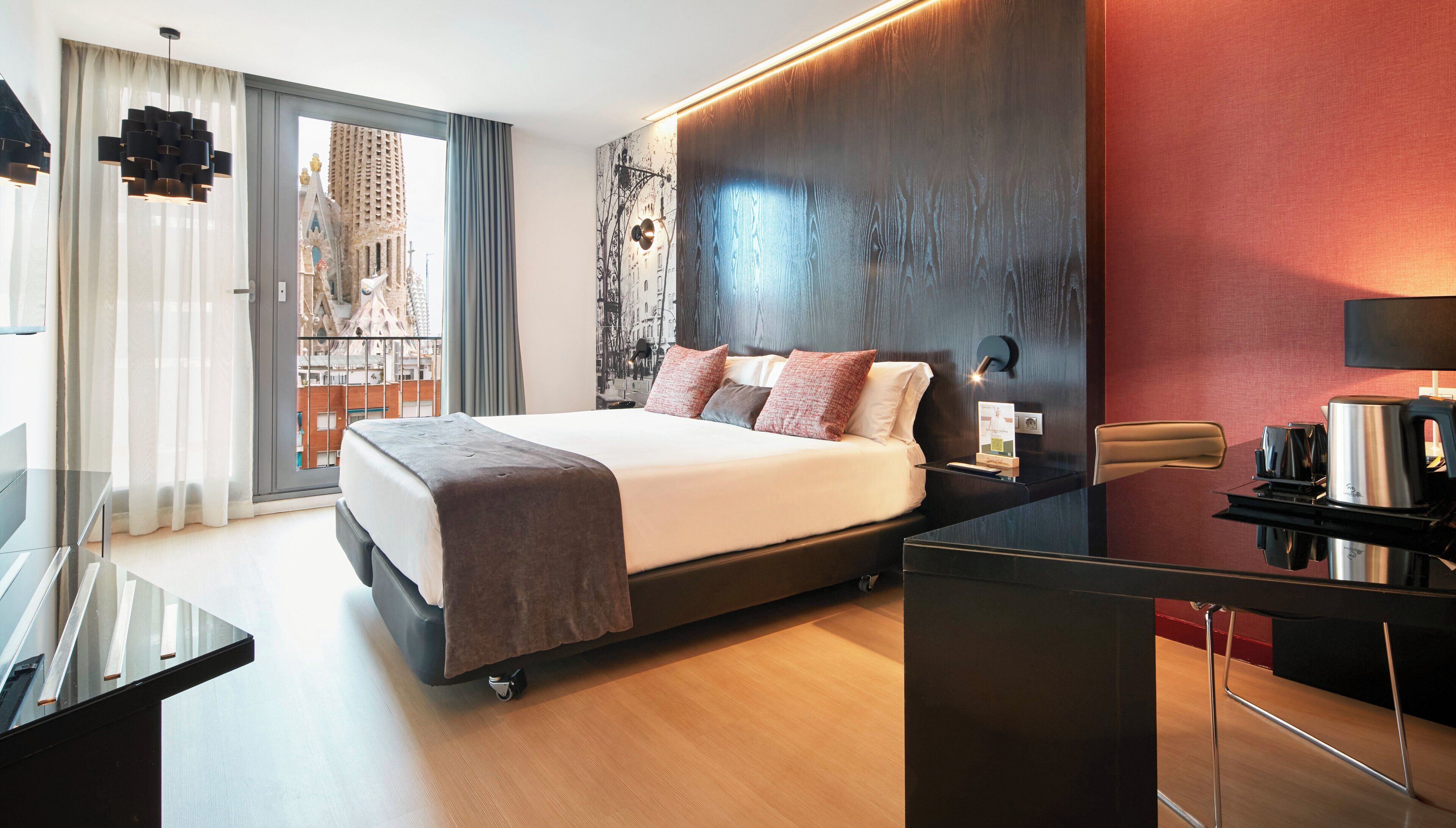 A modern hotel room with a large bed, a desk with a coffee maker, and a view of a cityscape through the window.