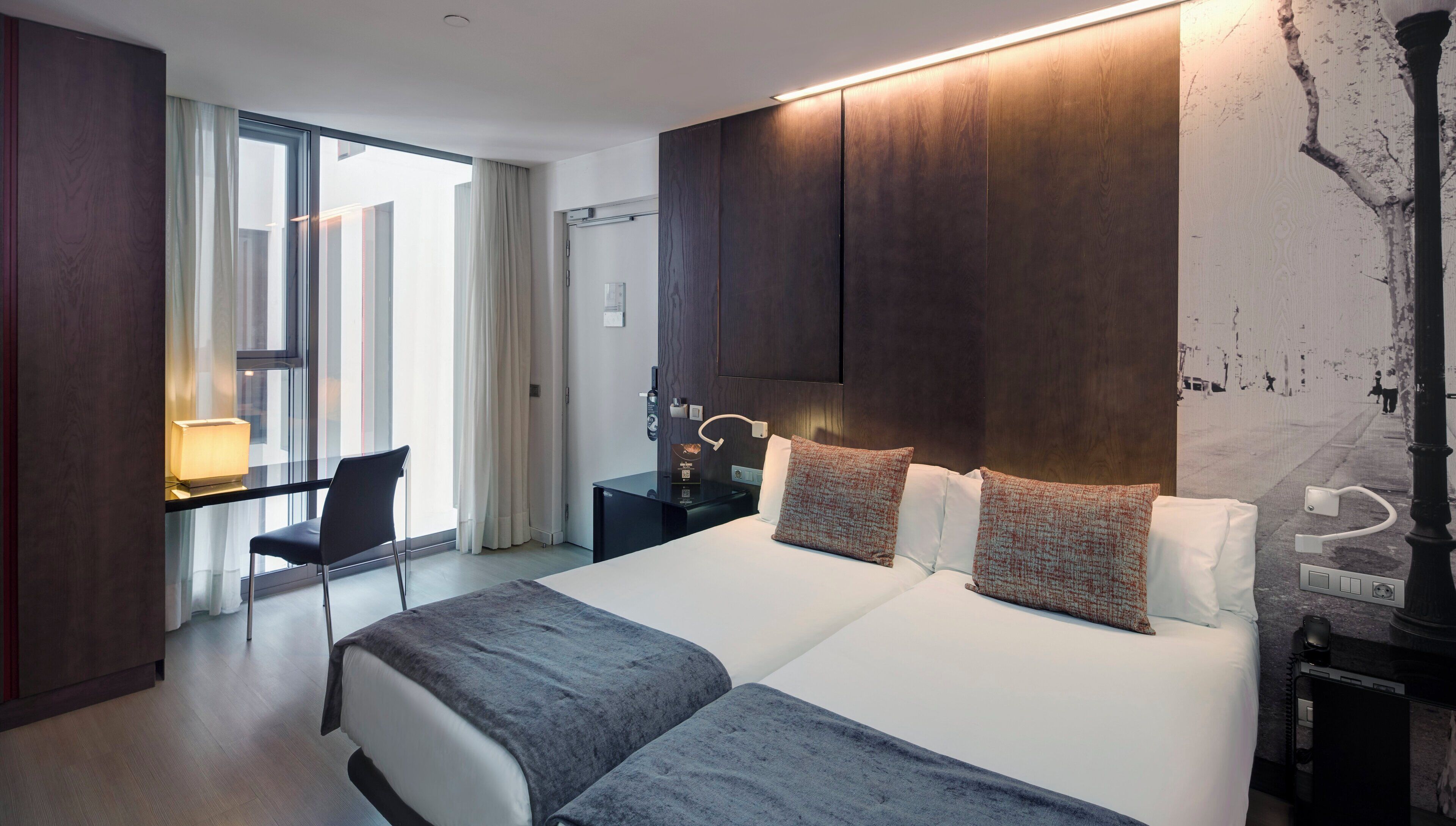 A modern hotel room with a large bed, bedside tables, a desk, and a chair.