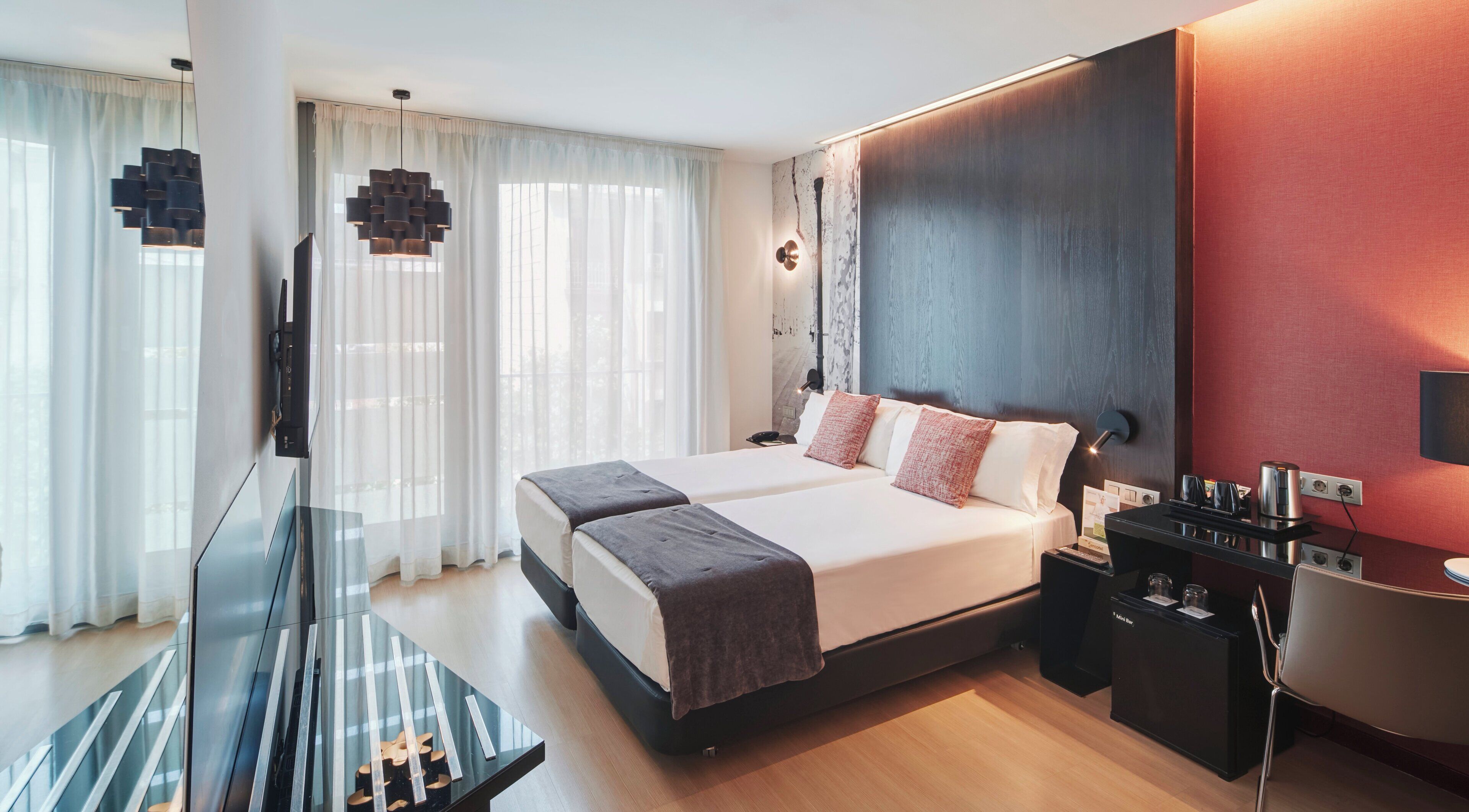 Ein modernes Hotelzimmer mit einem großen Bett, einem Schreibtisch mit Stuhl, einem Fernseher und einer Minibar.