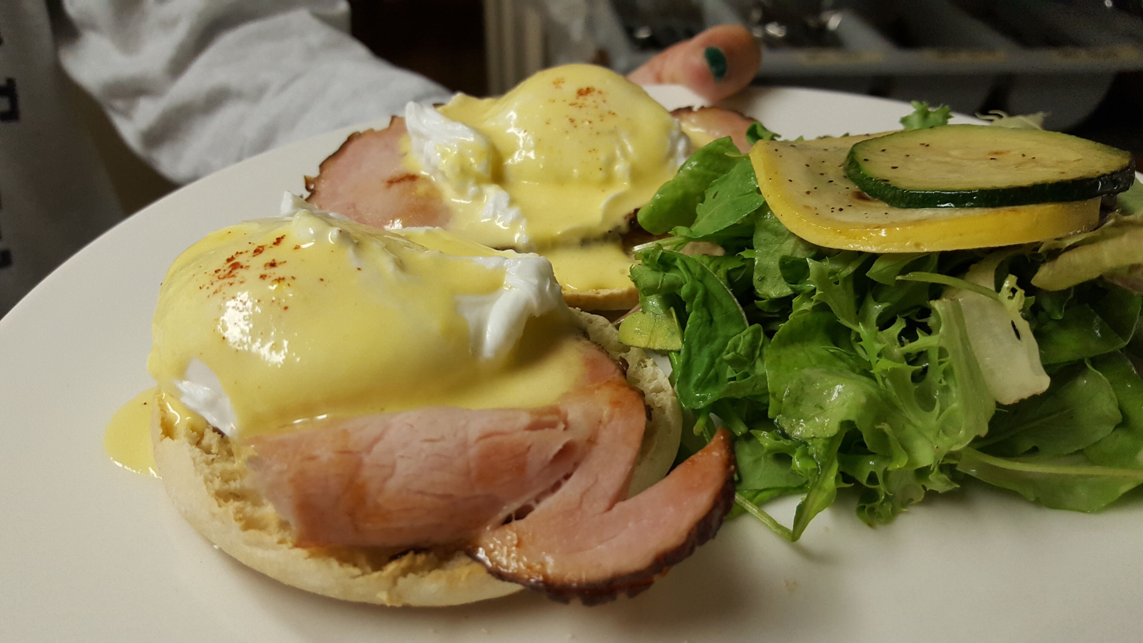 Un plato con huevos Benedictinos, jamón y una ensalada.