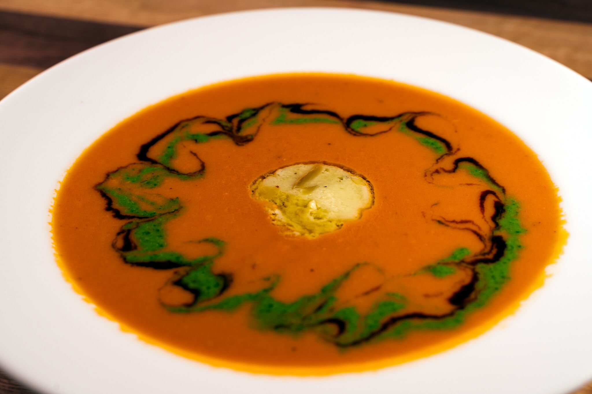A bowl of soup with a dollop of cream in the center, surrounded by a swirl of green sauce.