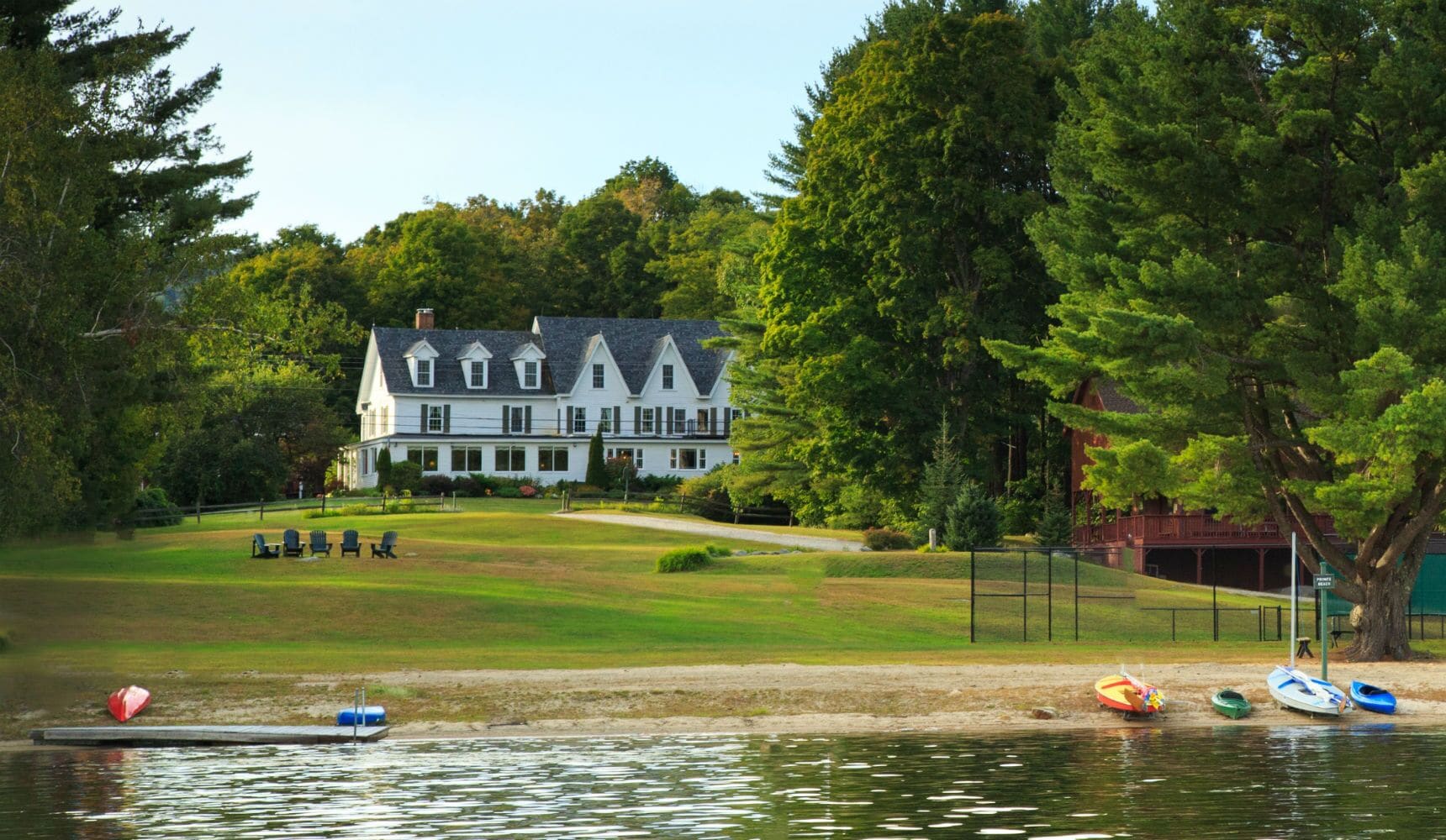 A large white house with a lawn and a lake.