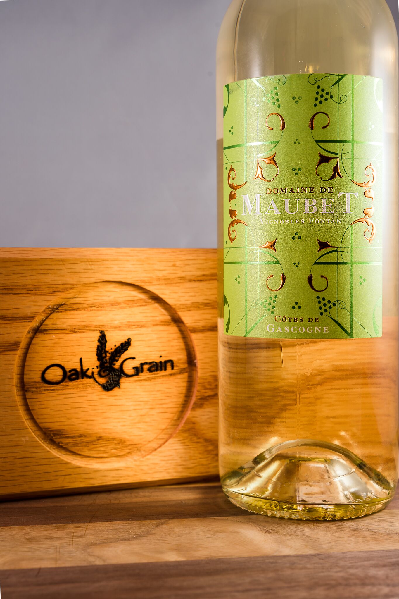 A bottle of Maubei wine with a green label, placed next to a wooden box with a circular design.