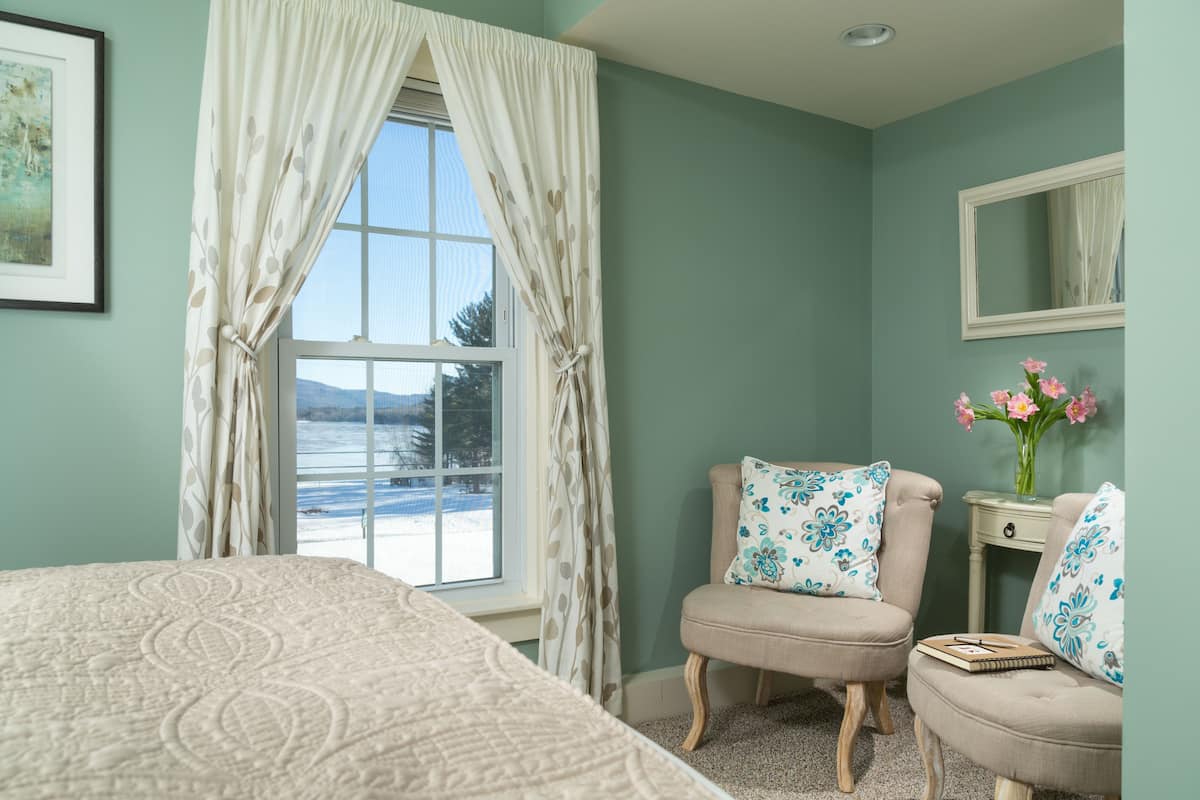 A bedroom with a bed, a chair, a nightstand, a mirror, and a window with curtains.
