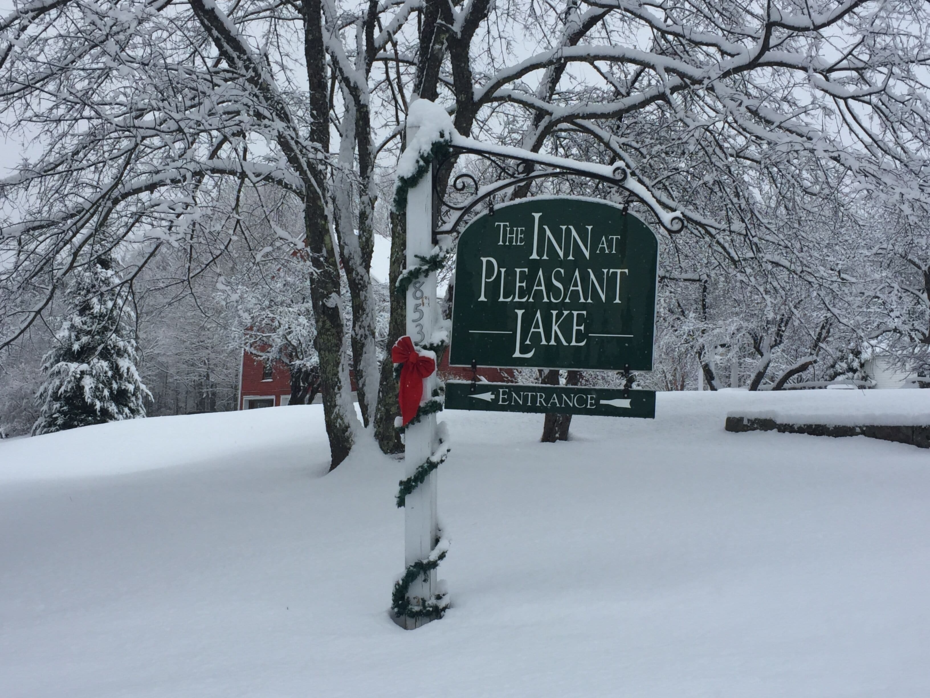 A snow-covered sign for The Inn at Pleasant Lake with an entrance arrow.