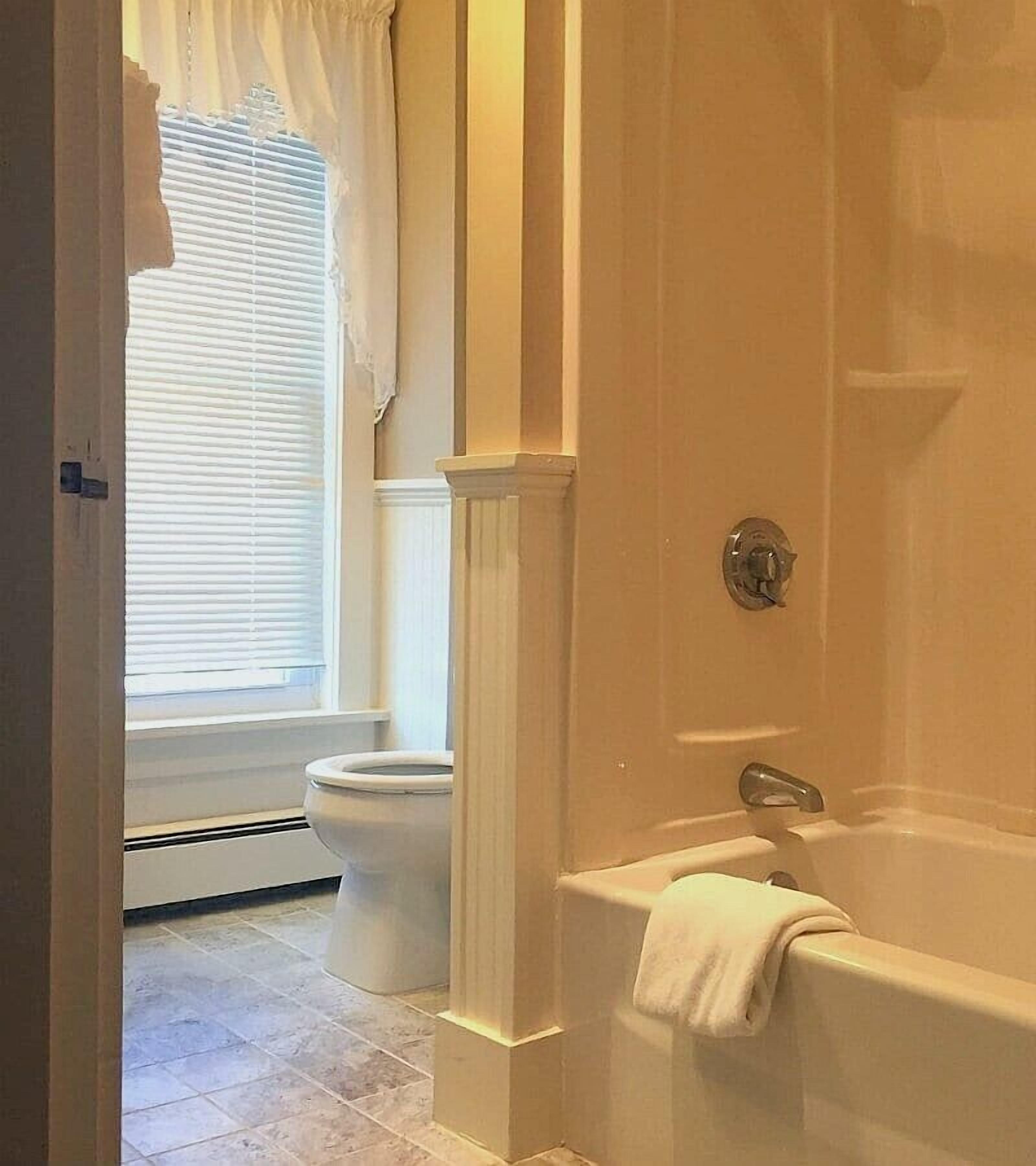 A bathroom with a bathtub, toilet, and window with blinds.