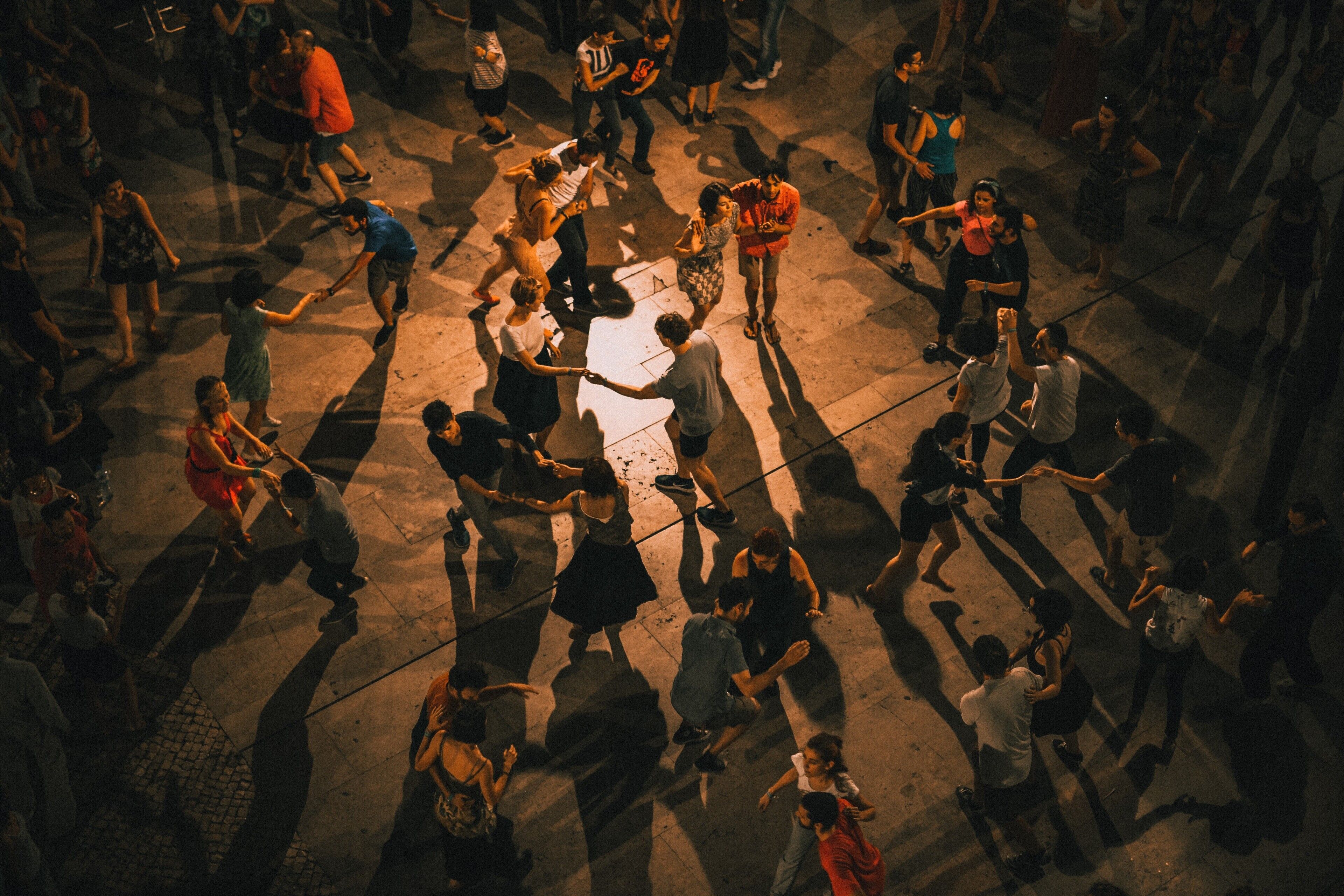 A crowded square with people gathered around a central point, possibly a fountain or monument.