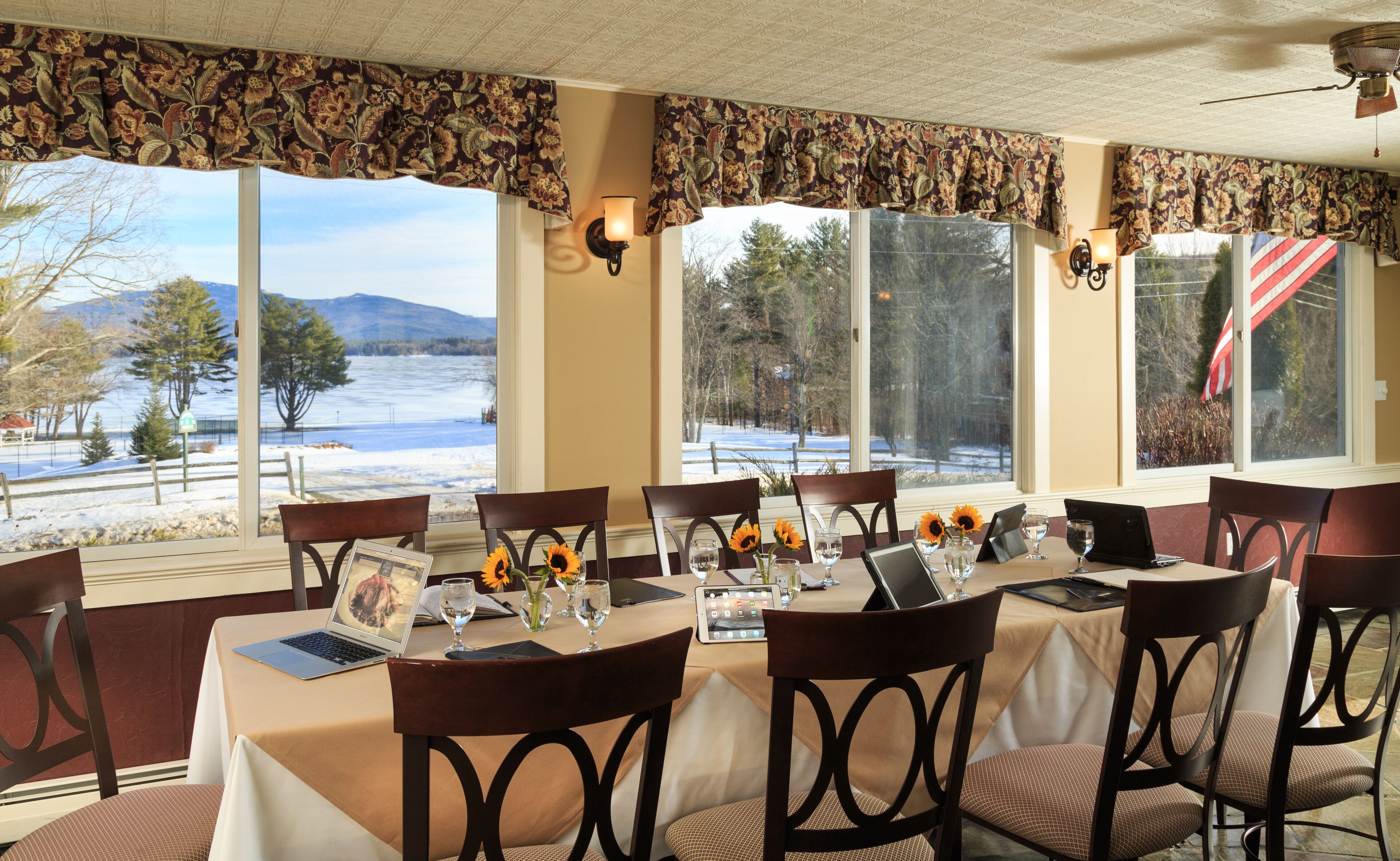 A dining area with a table set for six, large windows with a view of a snowy landscape, and a ceiling fan.