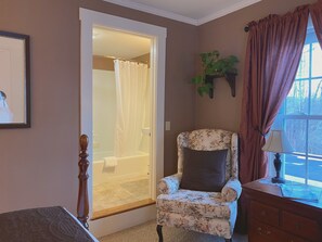 A bathroom with a shower, a floral armchair, and a wooden dresser.